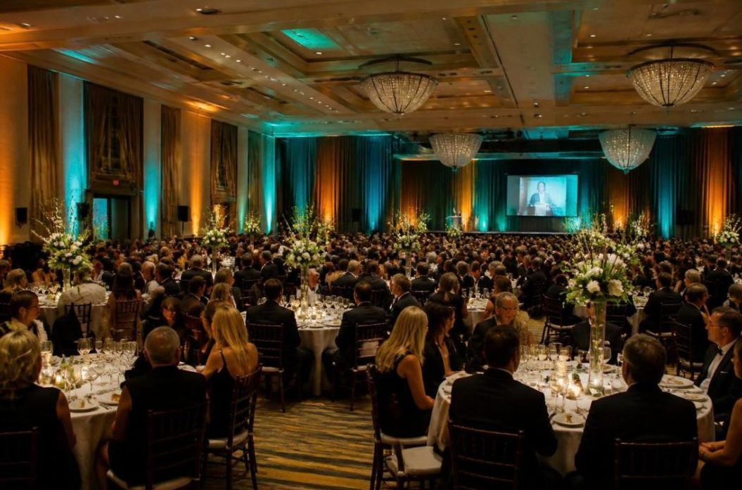 Fundraising gala in a hotel ballroom with round tables and teal uplighting